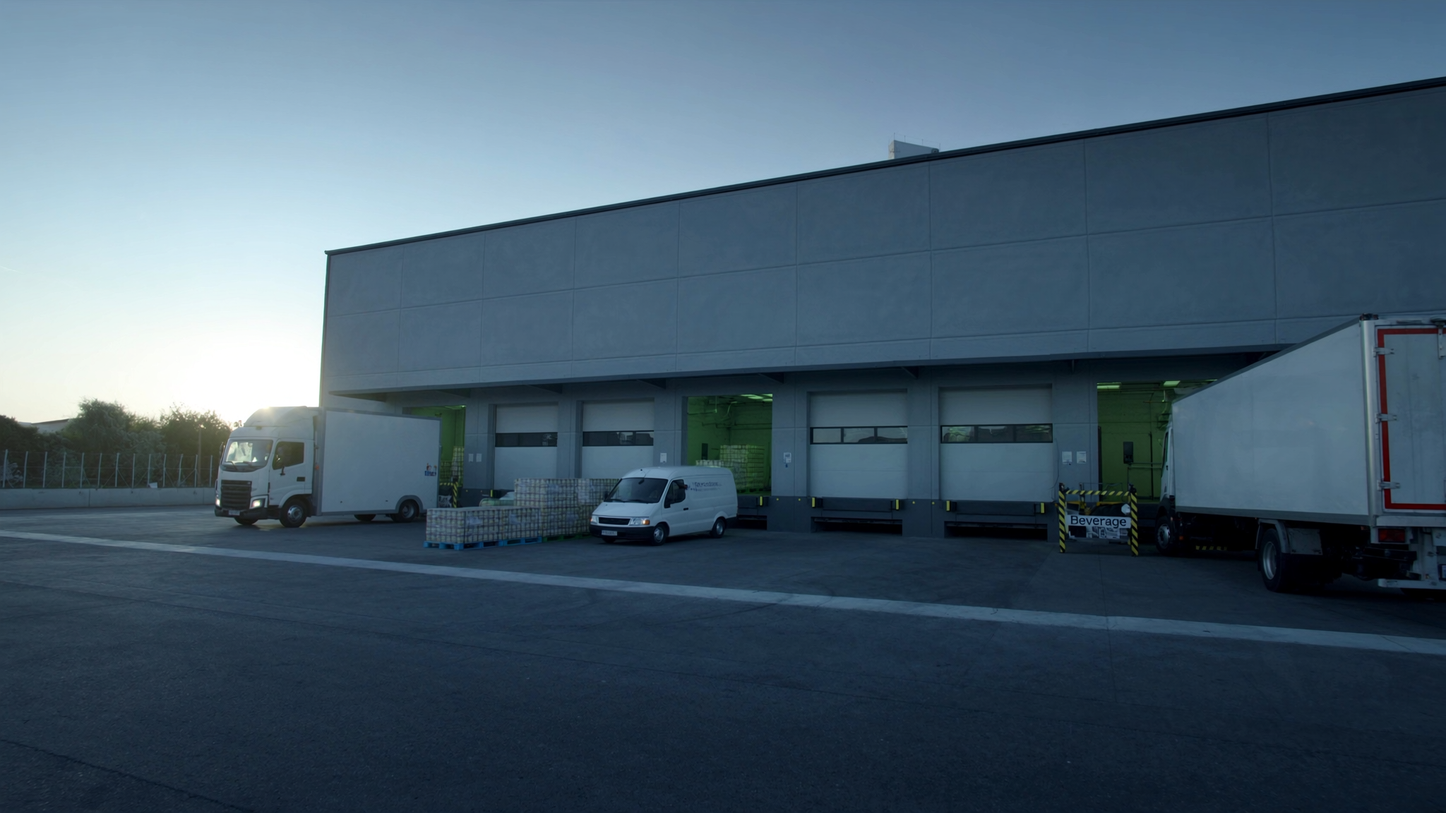 Beverage distribution warehouse loading dock at dawn with route delivery trucks lined up — illustrating the operational challenges beverage distributors face